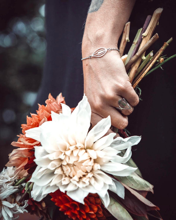 Blombukett med vita och orangea blommor, en hand med guldsmycken håller i den mjukt.